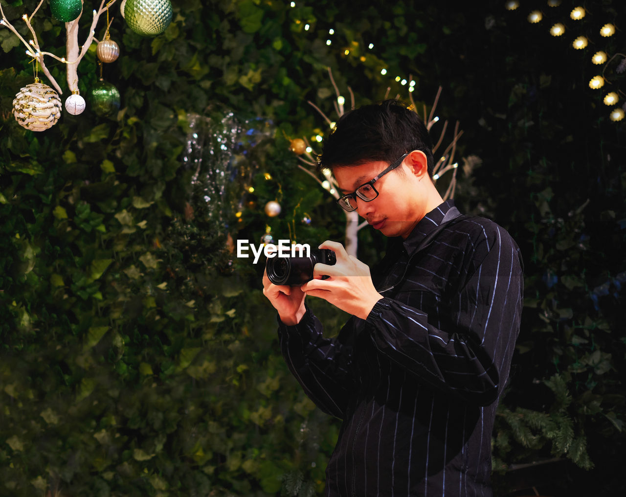 Low angle view of young man taking picture on camera by christmas tree