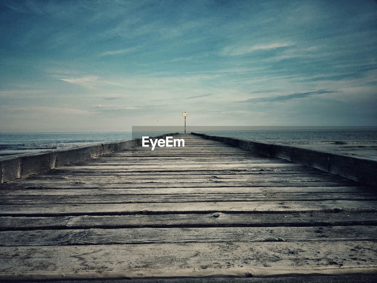 Wooden boardwalk amidst sea against cloudy sky