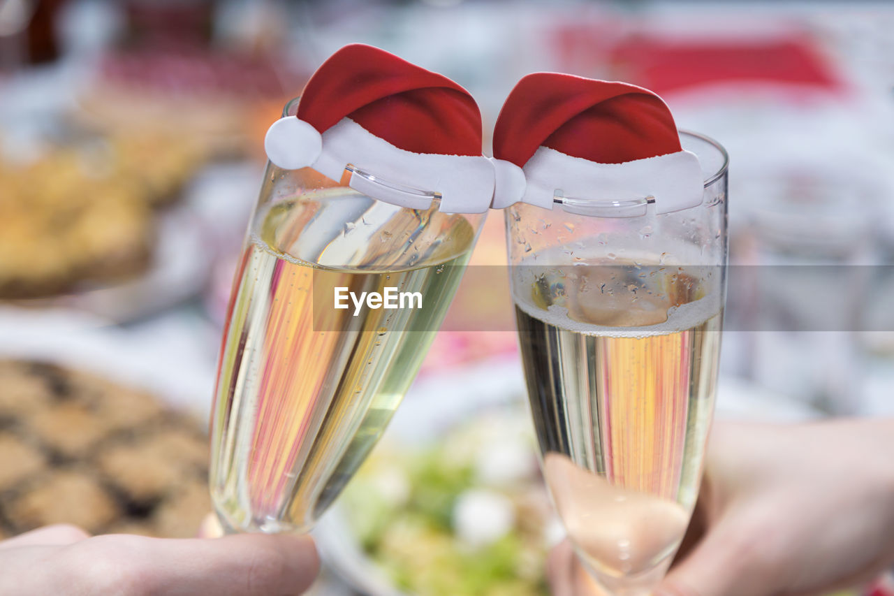 Cropped hands of friends toasting champagne flutes with santa hats at table