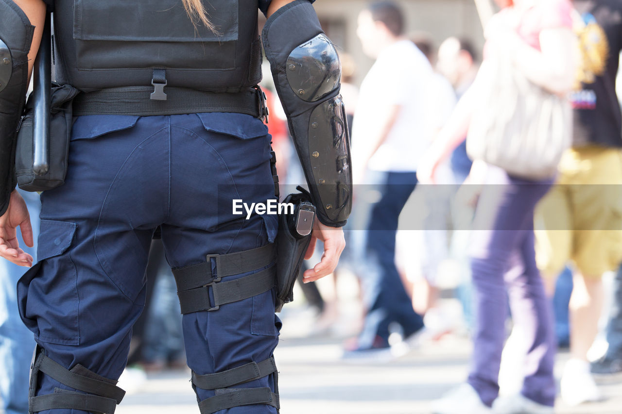 Rear view midsection of female police officer standing with hand on hip