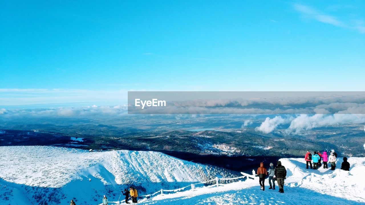 High angle view of people standing on snow covered mountain against blue sky