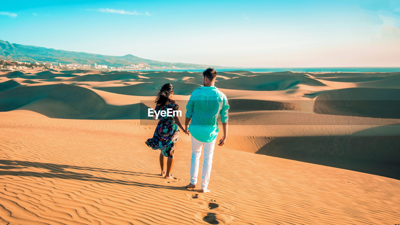 rear view of man walking on sand at desert