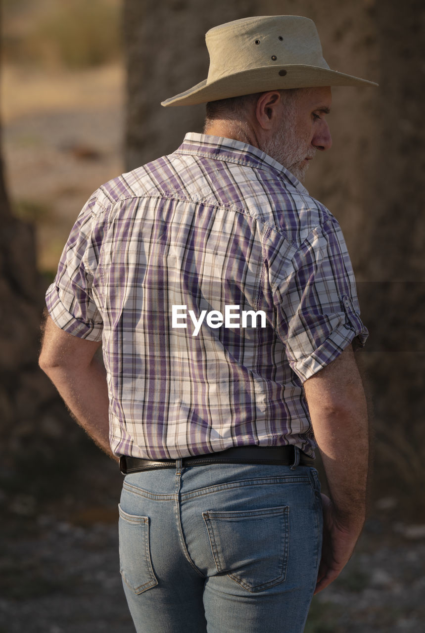 Rear view of adult man in cowboy hat and shirt against abandoned building