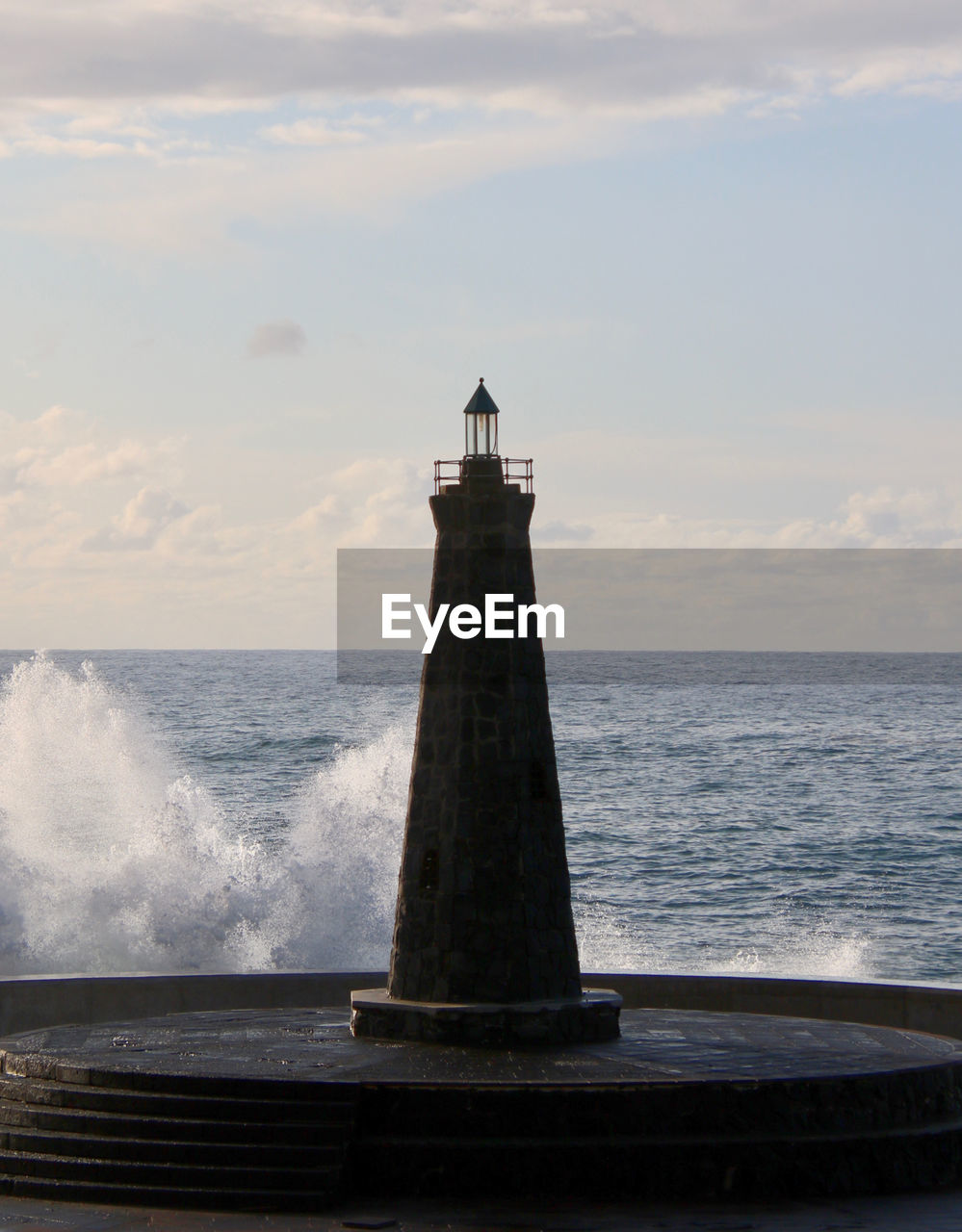 Lighthouse against sky, waves crashing in from sea