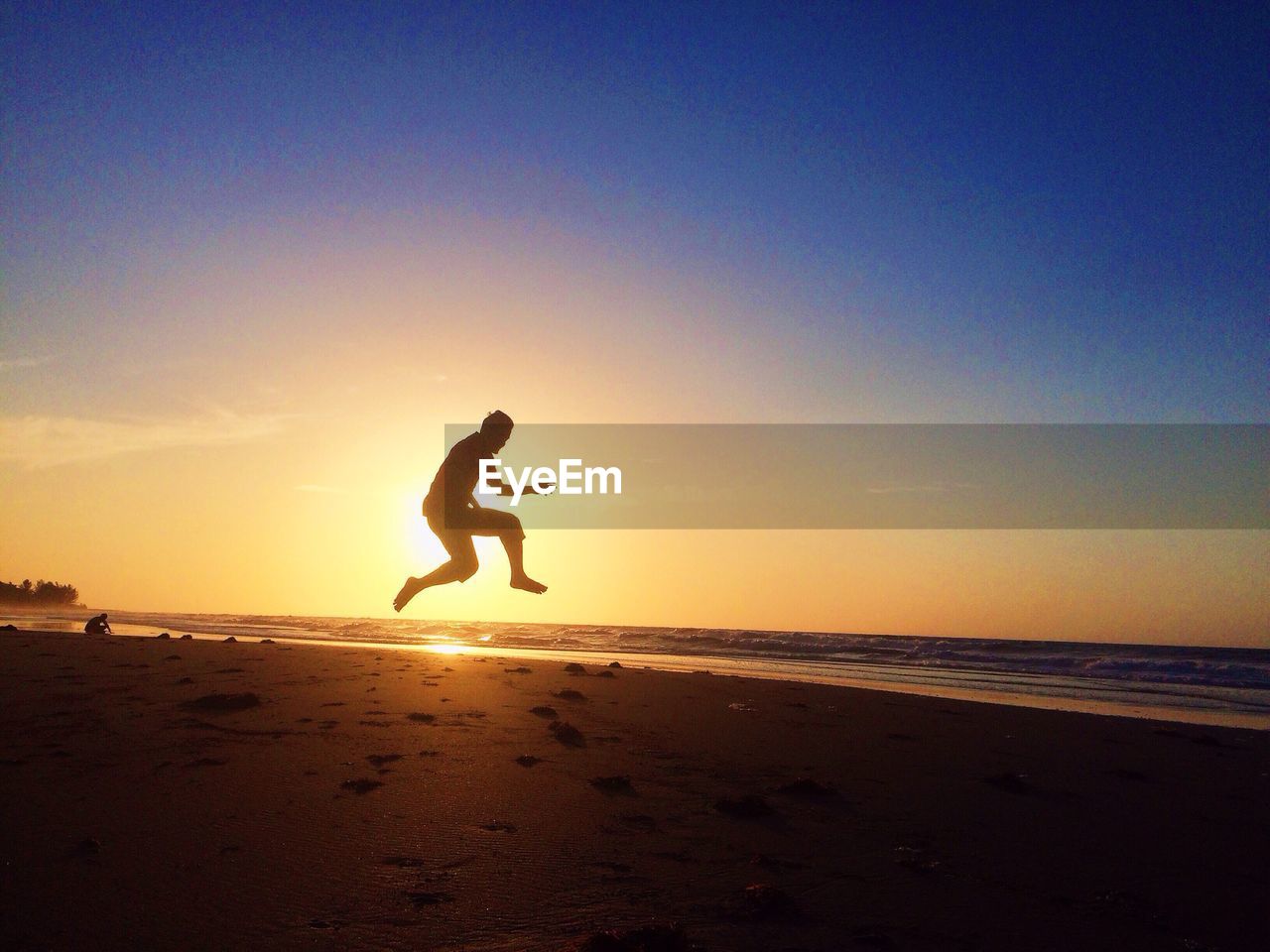 Full length of silhouette man jumping at beach against clear sky during sunset