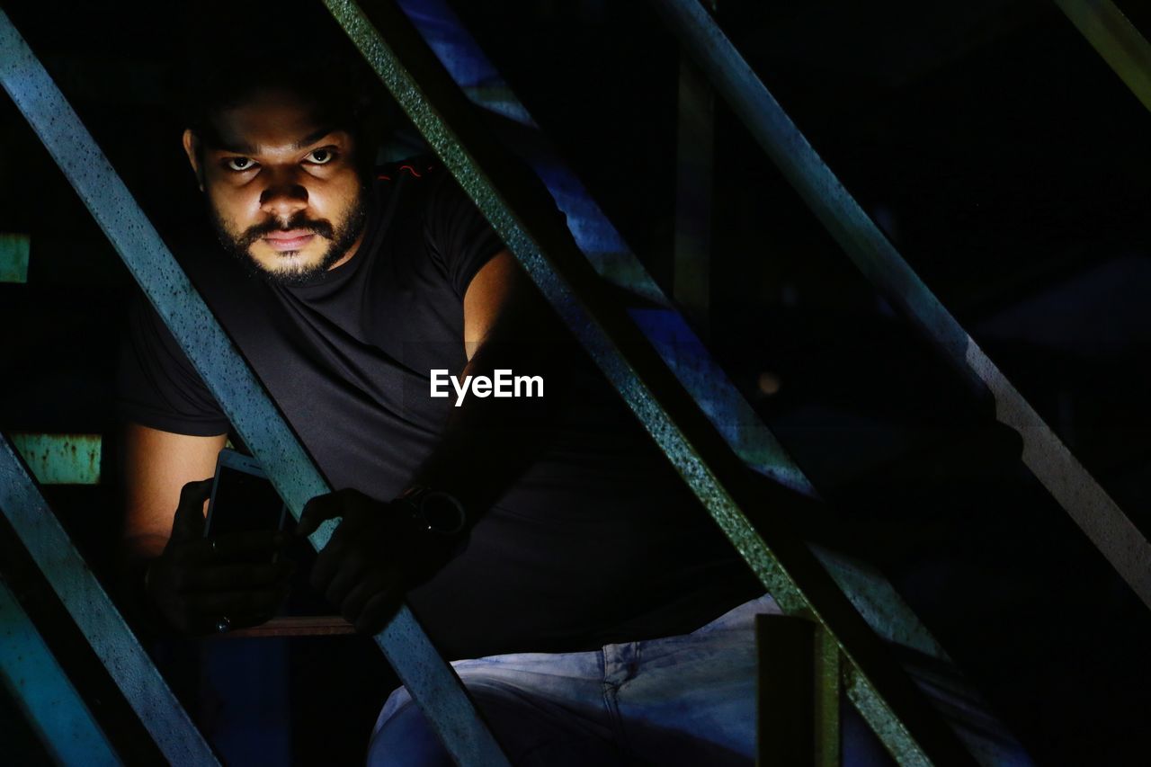 Portrait of young man in front of metal gate at night