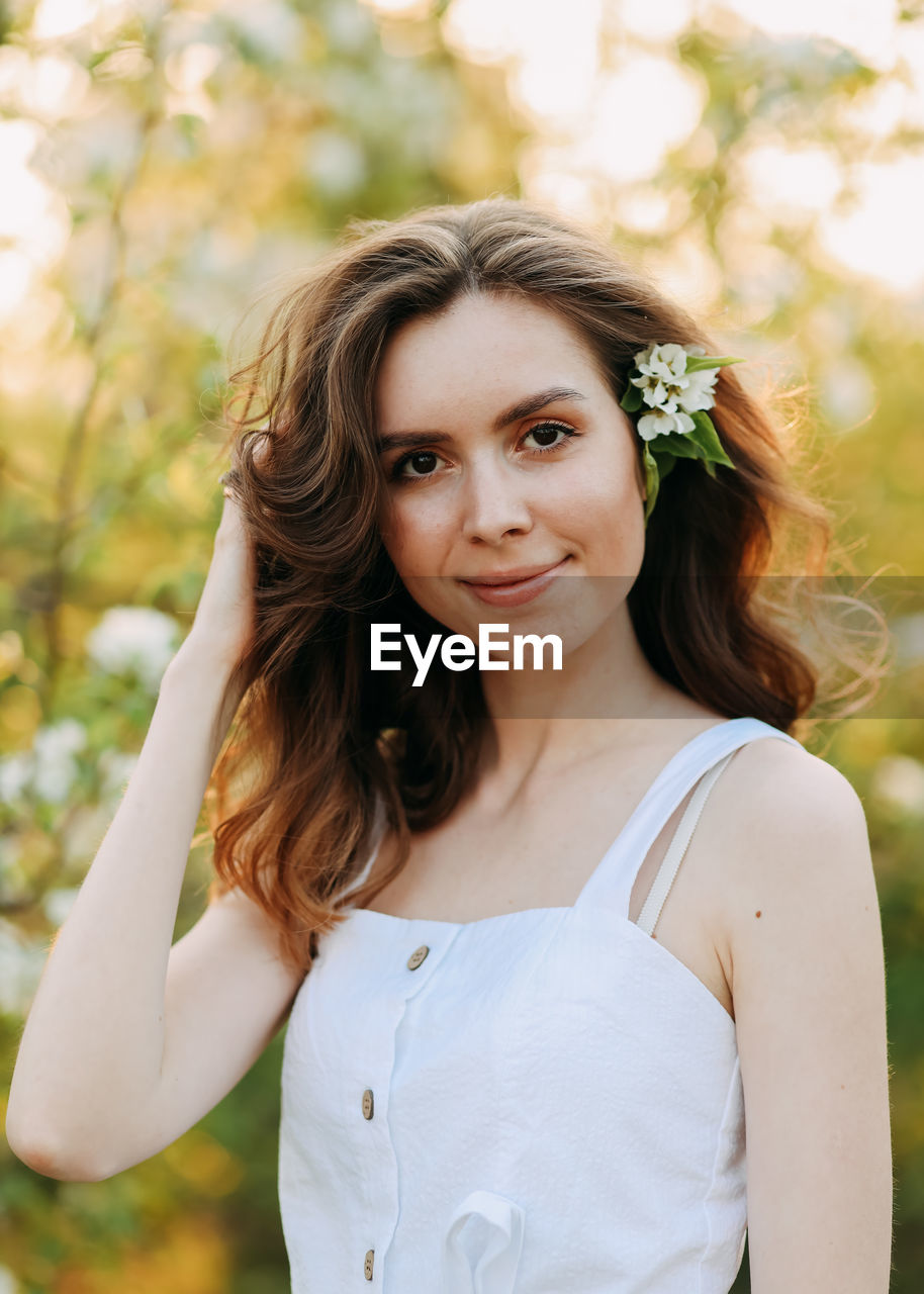 A cute happy young woman with a hairstyle in a white dress is walking enjoying nature in the summer