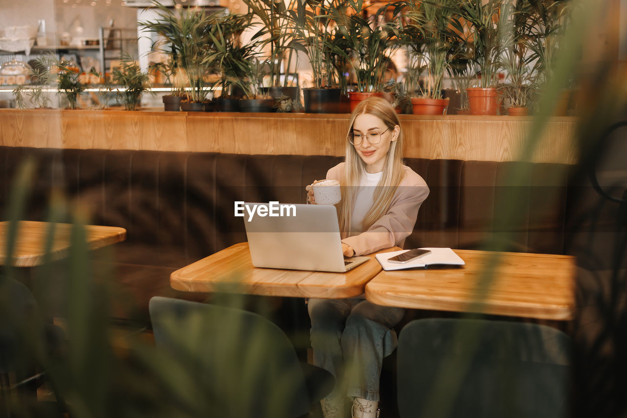 A business woman with glasses works online using a laptop. shot through a window