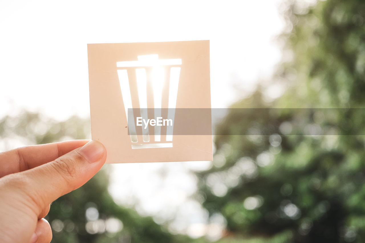 Cropped hands of person holding paper against sky