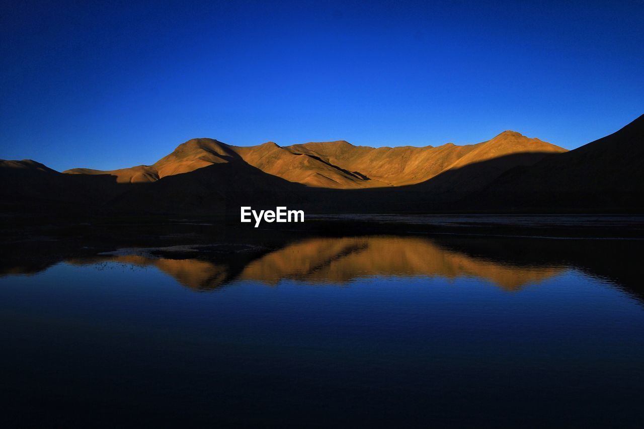 Scenic view of lake and mountains against clear blue sky