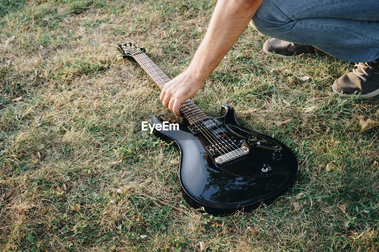 Low section of man picking up electric guitar on grassy field