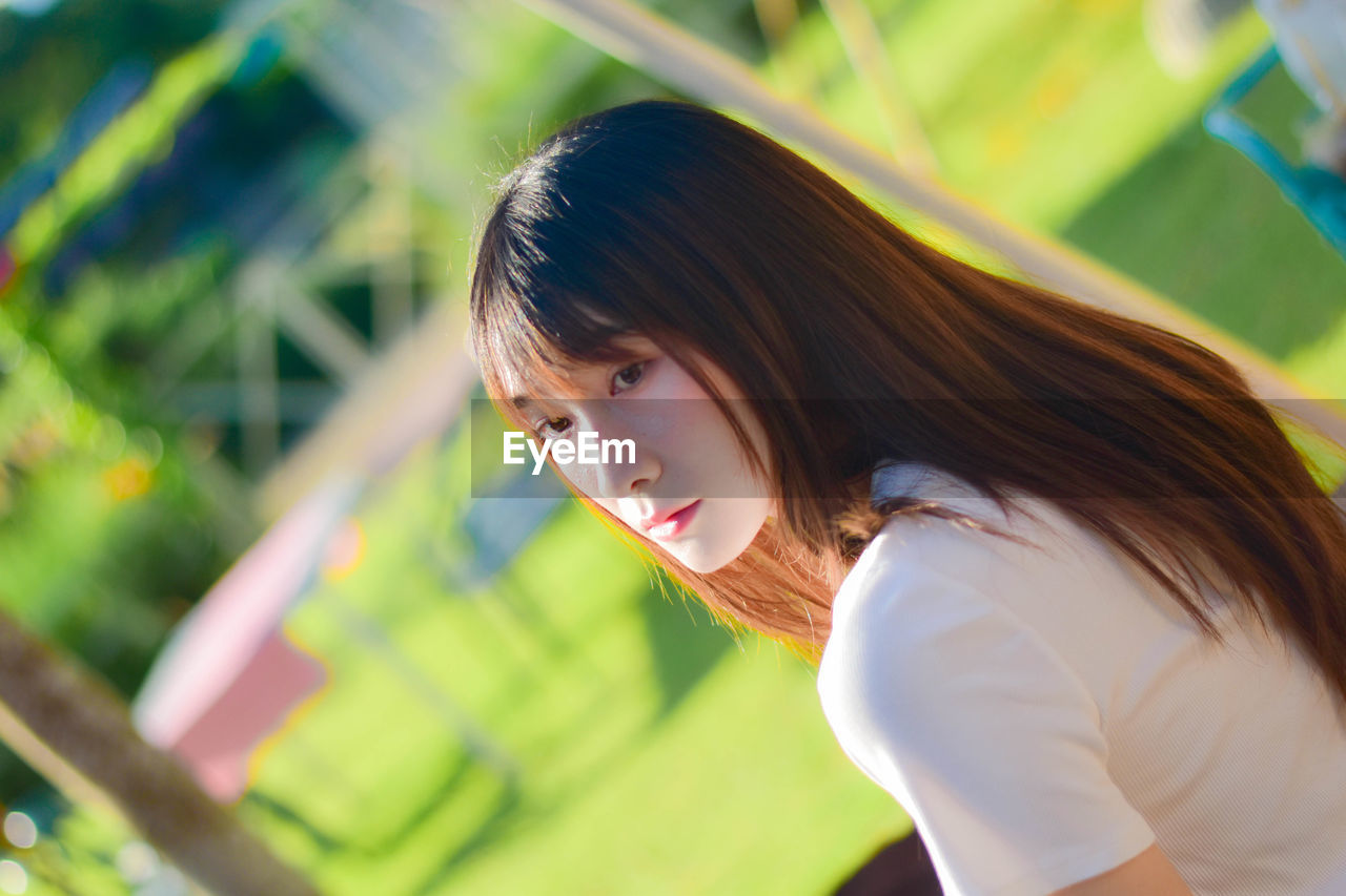 young woman looking away against trees