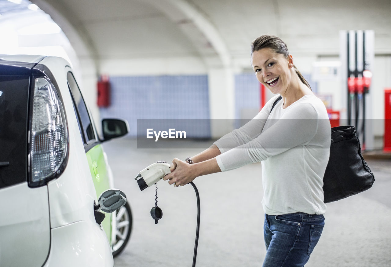 Side view portrait of playful woman electrical charger pump at gas station