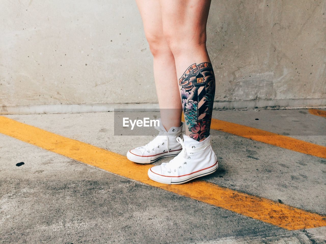 Low section of woman with tattoo standing on footpath