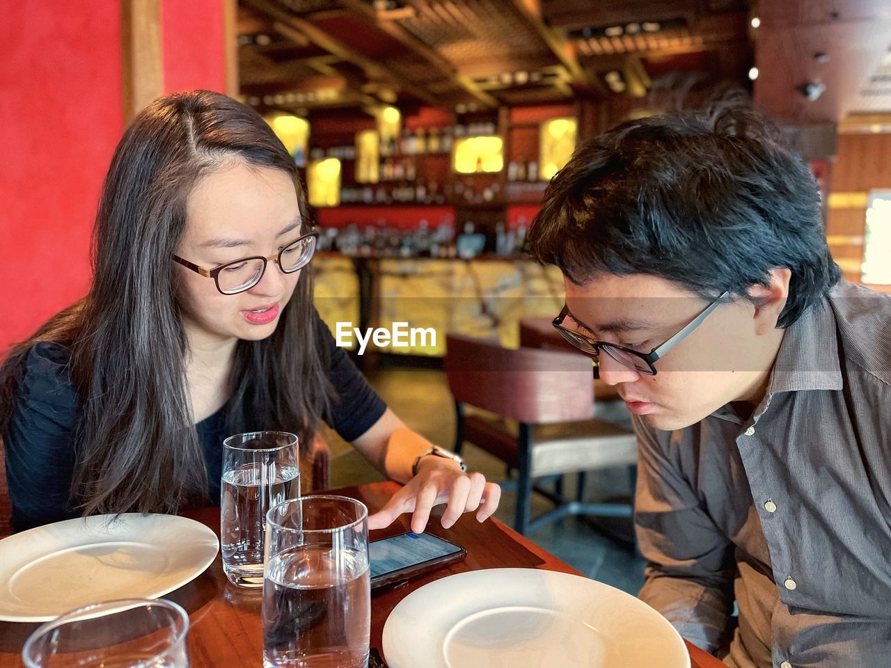 Side view of young asian man and woman in eyeglasses having a discussion over lunch in a restaurant.