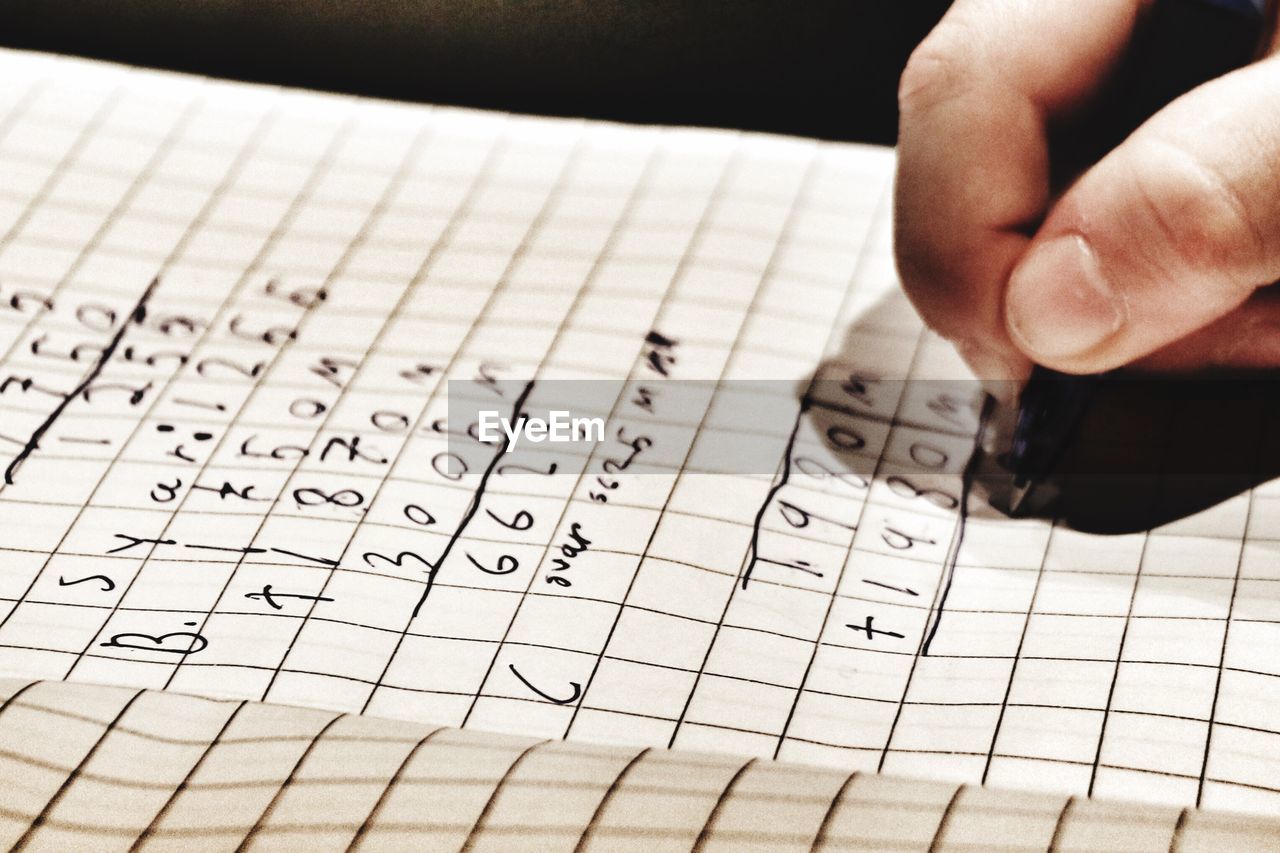 Cropped hand of person solving mathematics problems on paper