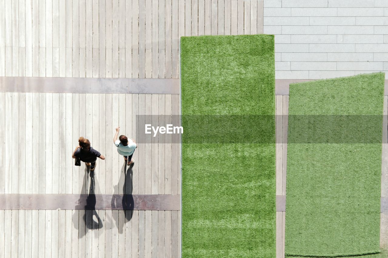 High angle view of people walking on wooden floor by green carpets