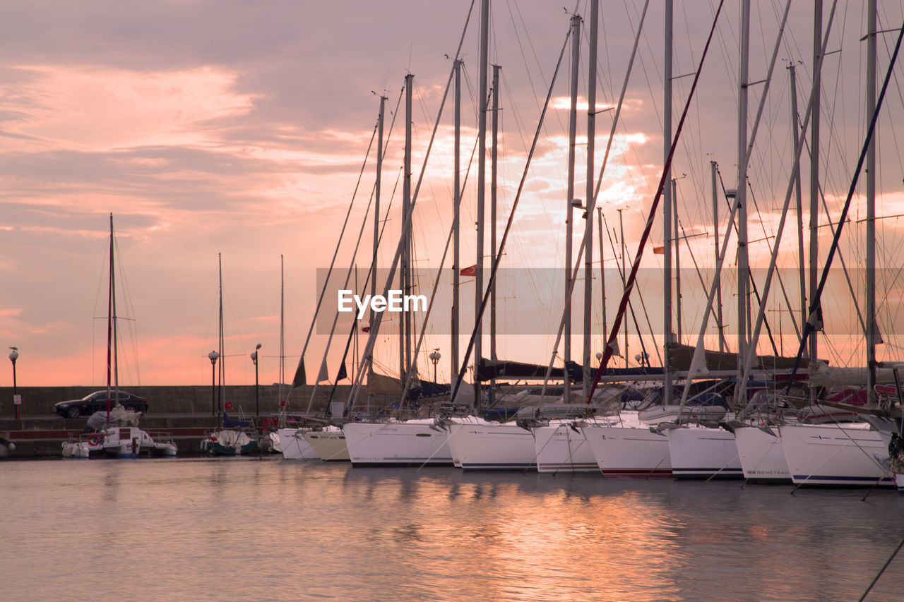 Boats moored at harbor against sky during sunset