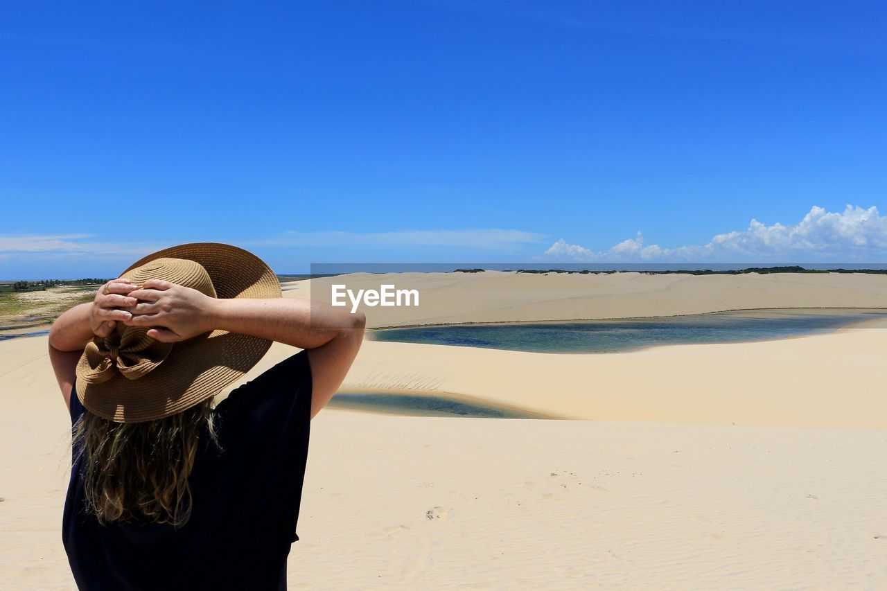 Rear view of woman wearing hat while standing at desert against blue sky