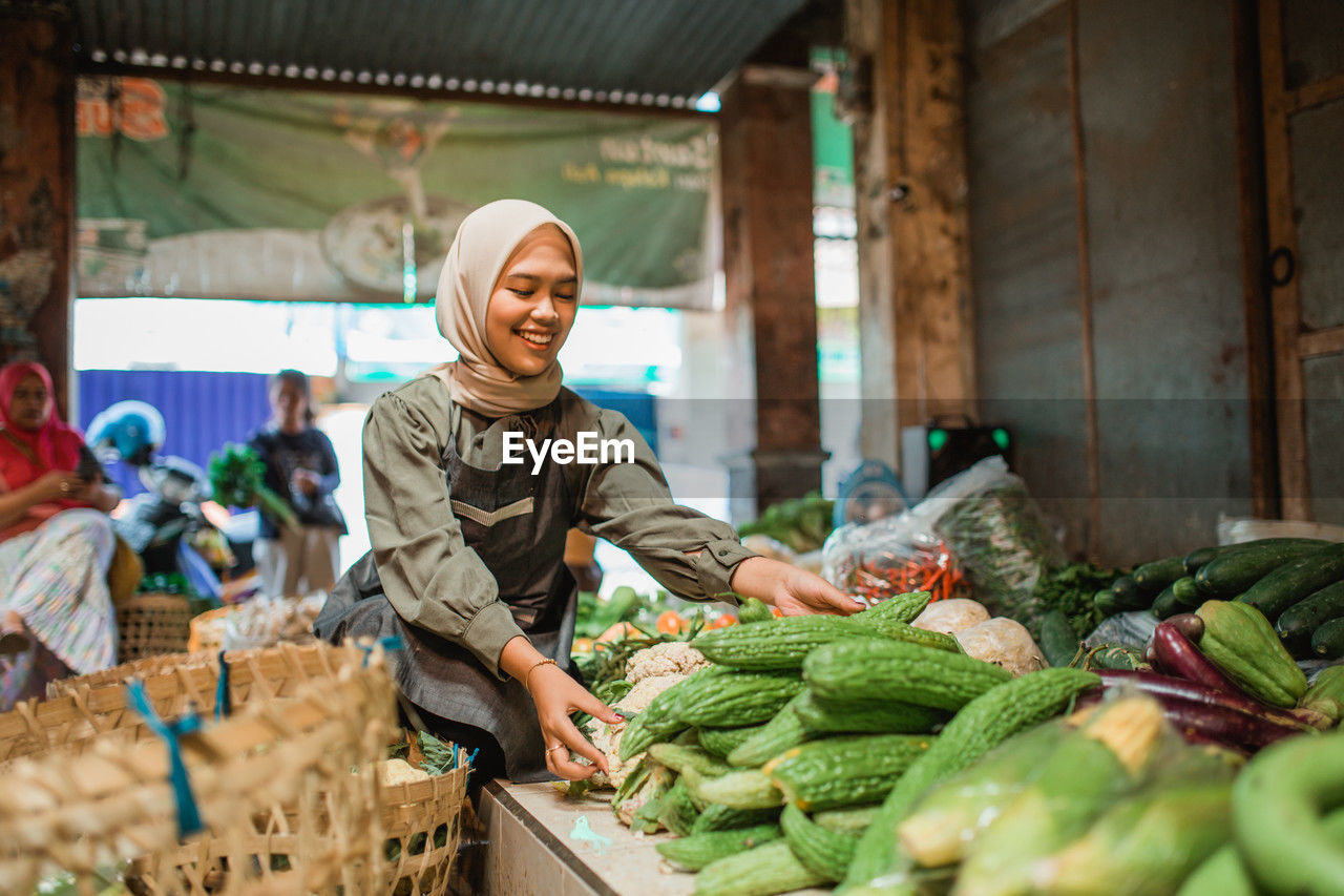 portrait of smiling young woman with vegetables in market