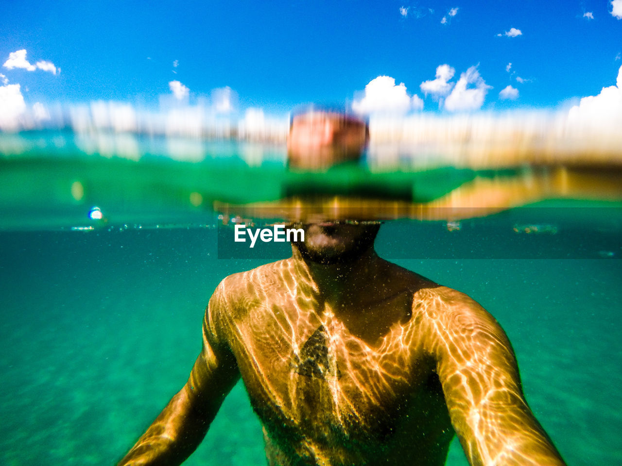 Shirtless man swimming in sea against sky