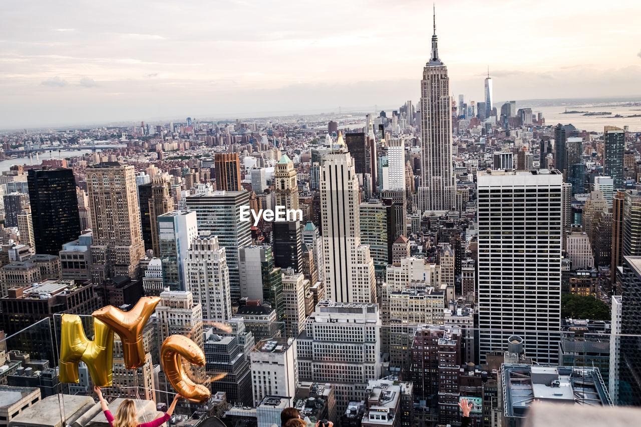 Rear view of woman holding alphabet balloons against empire state building in city
