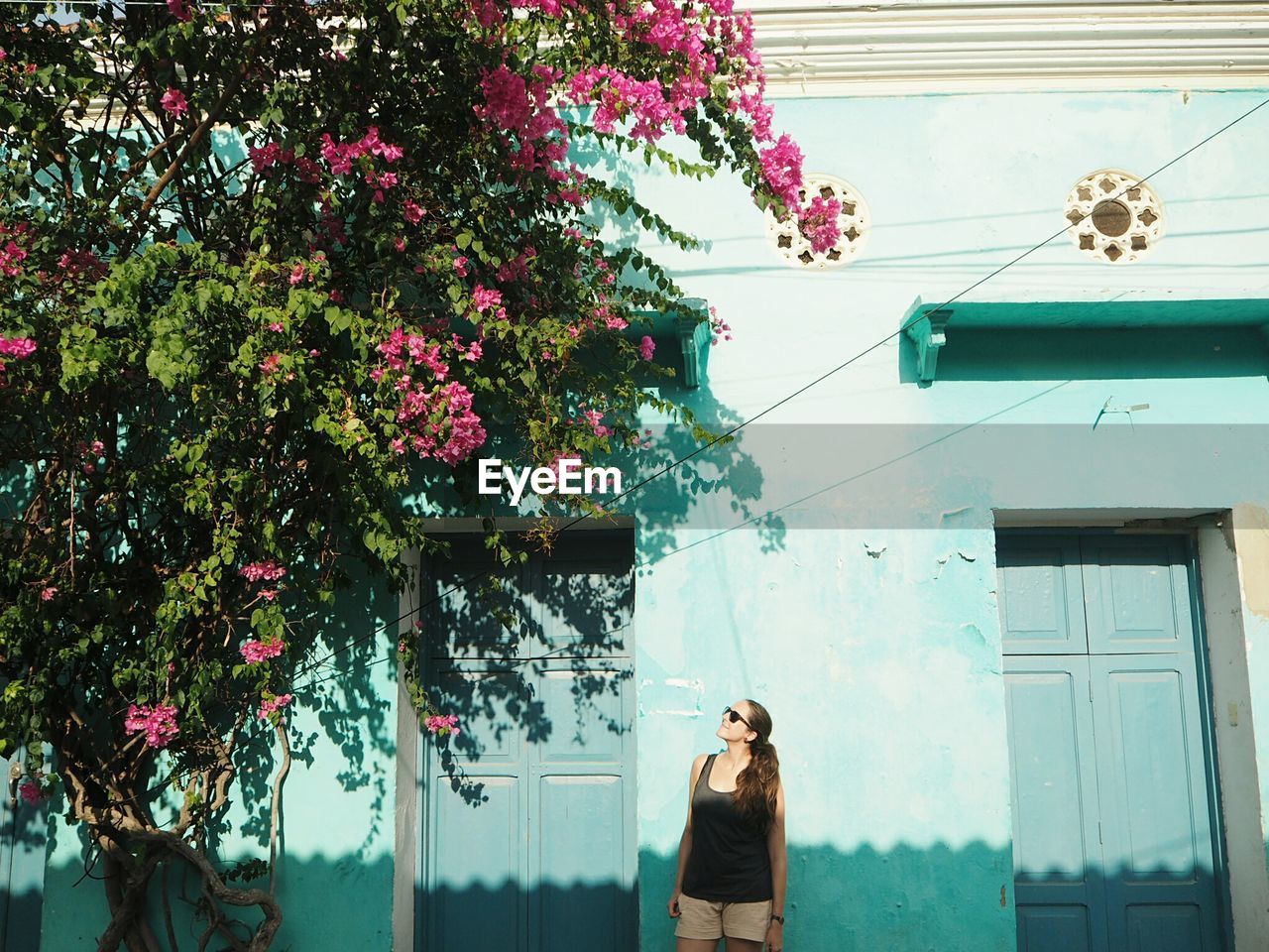 Woman standing against building while looking at tree