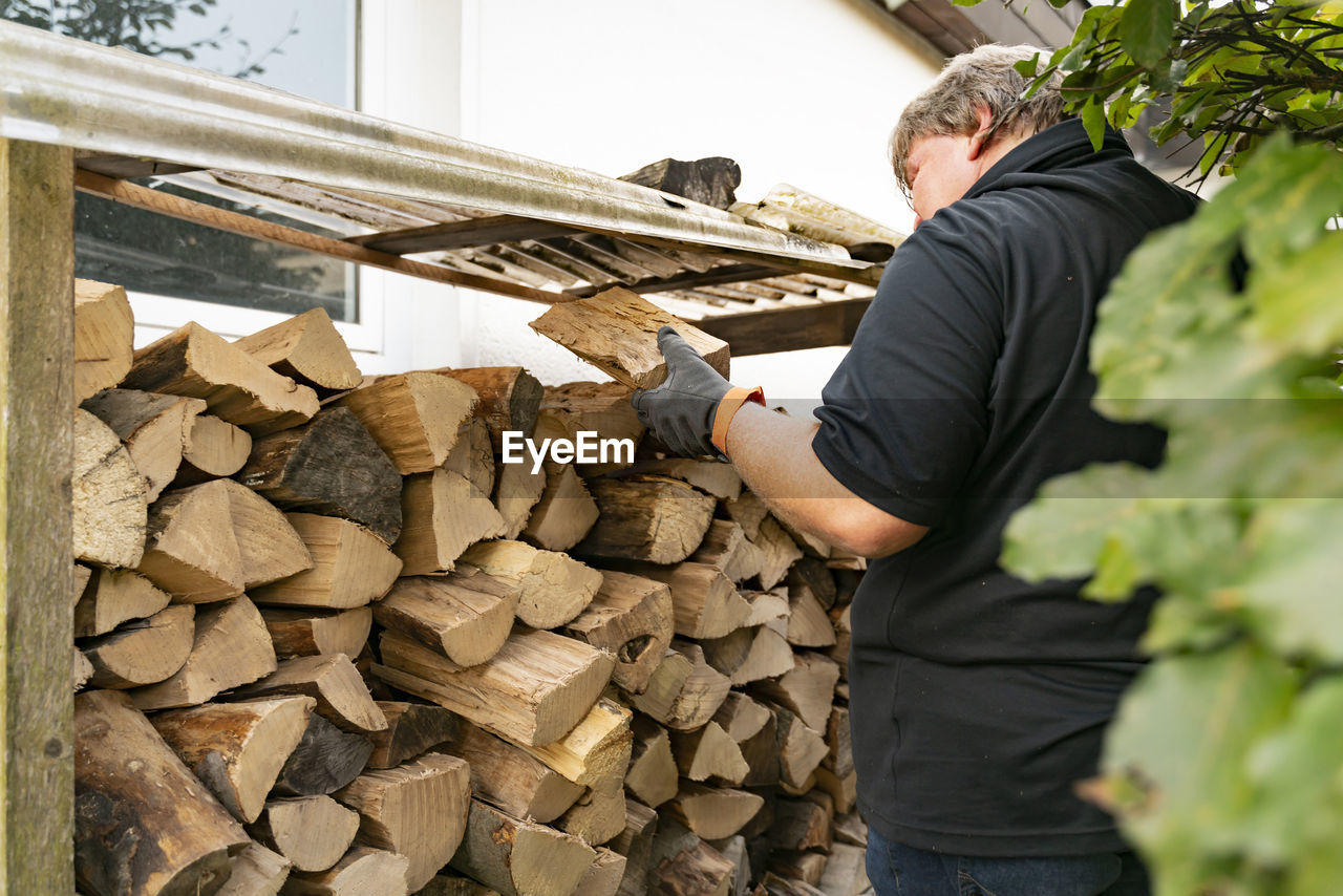 A 50 year old man has received a delivery of firewood and is putting the beech logs into the rack. 