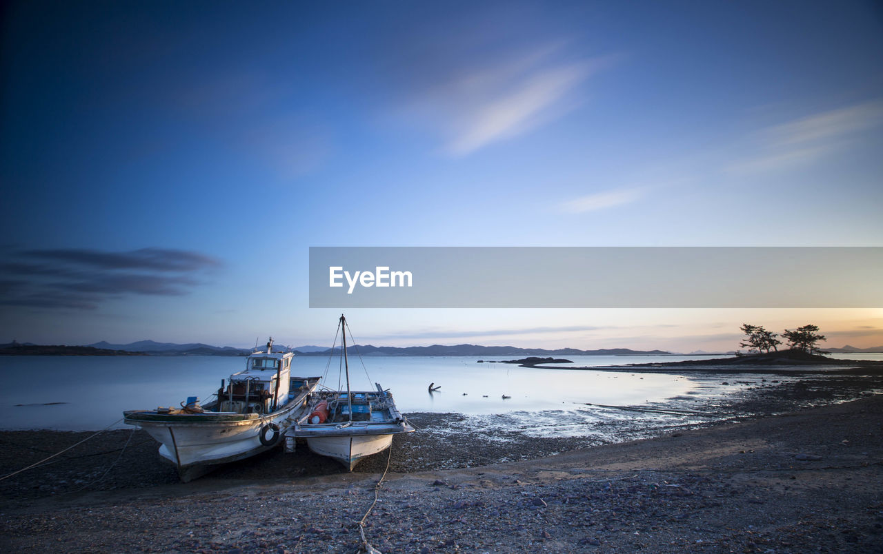 Sailboats moored on sea against sky during sunset