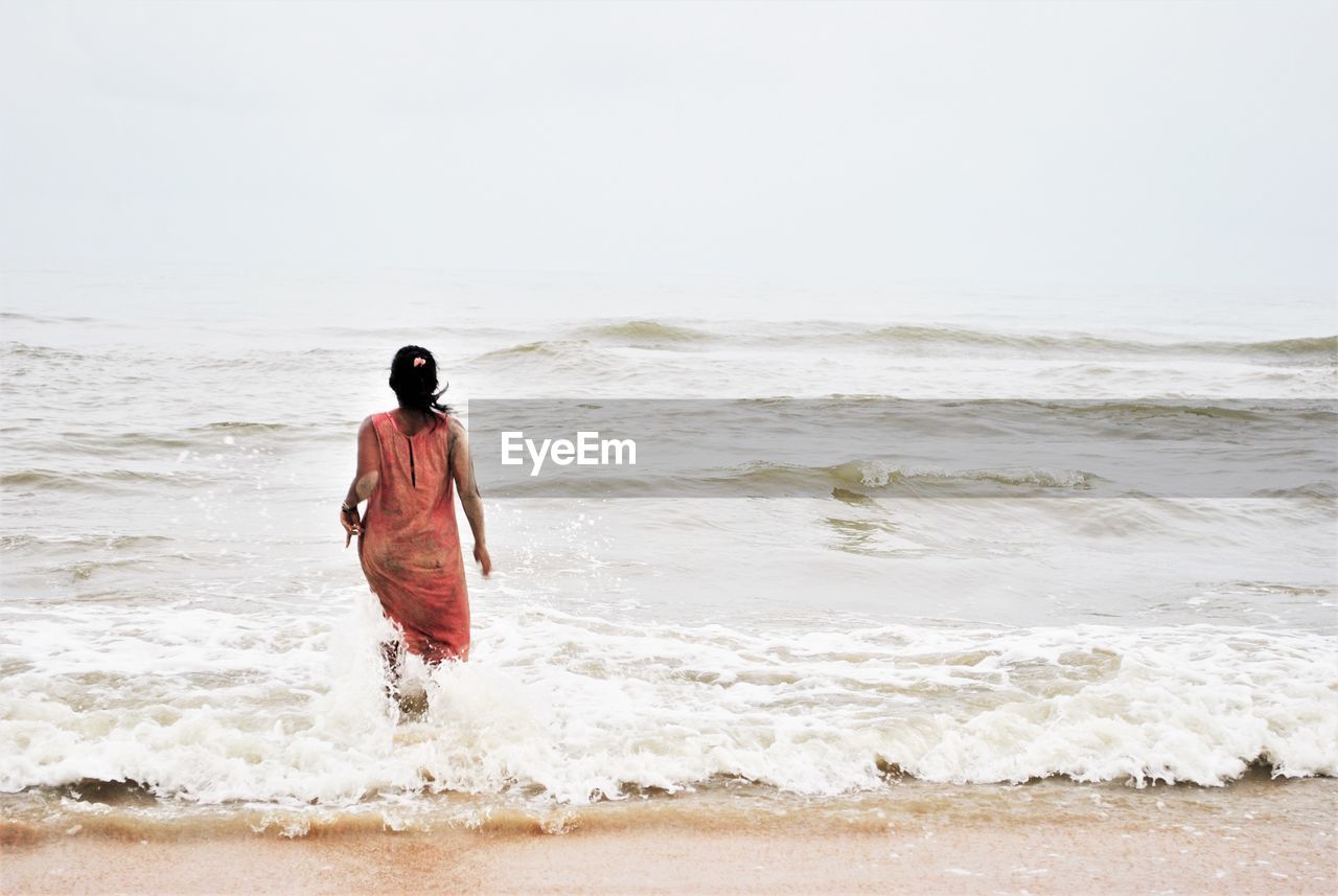 Rear view of woman walking on shore at beach against clear sky