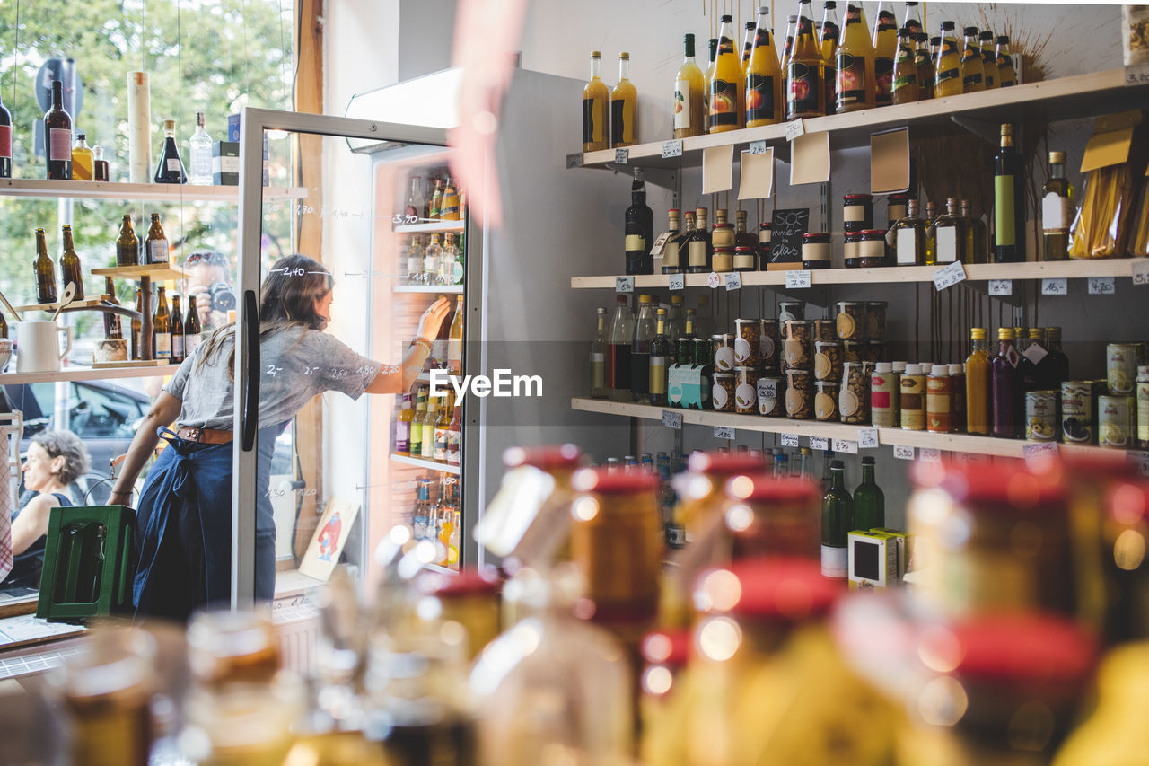 Female employee arranging bottles in refrigerator at deli