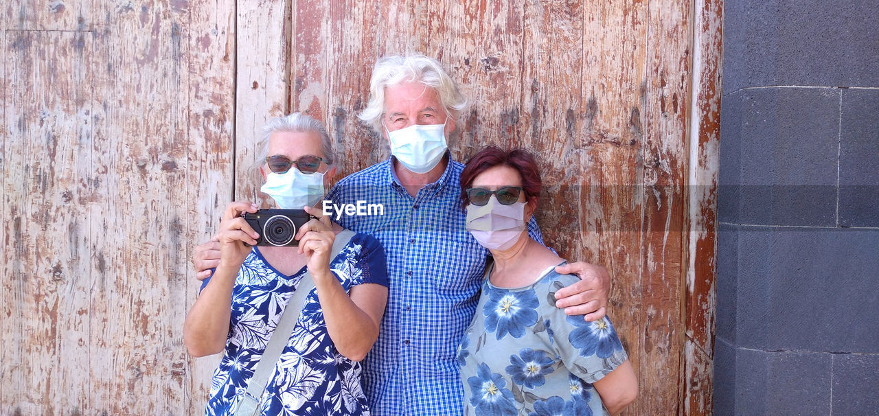 Portrait of friends wearing masks standing against wall