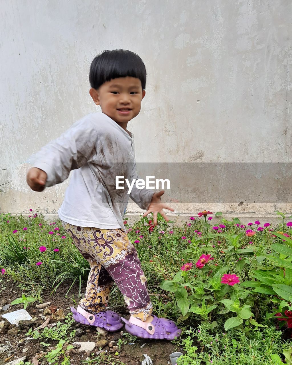 Side view of cute boy standing by flowering plants