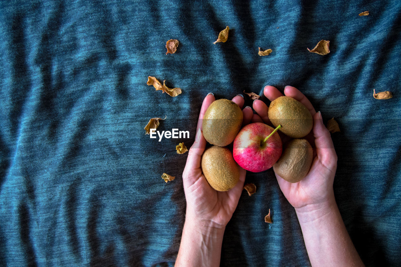 Cropped hands holding apple and kiwis on fabric