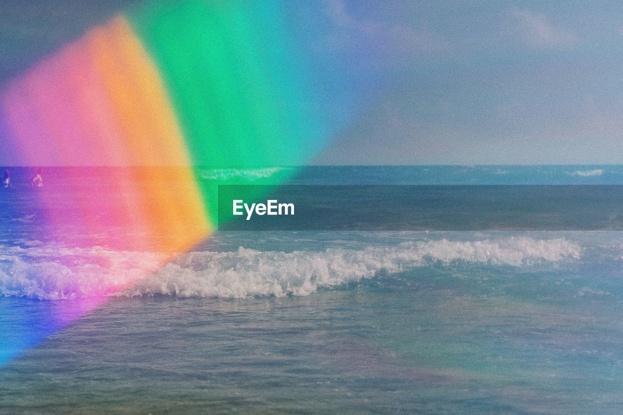 Digital composite image of rainbow over sea against sky