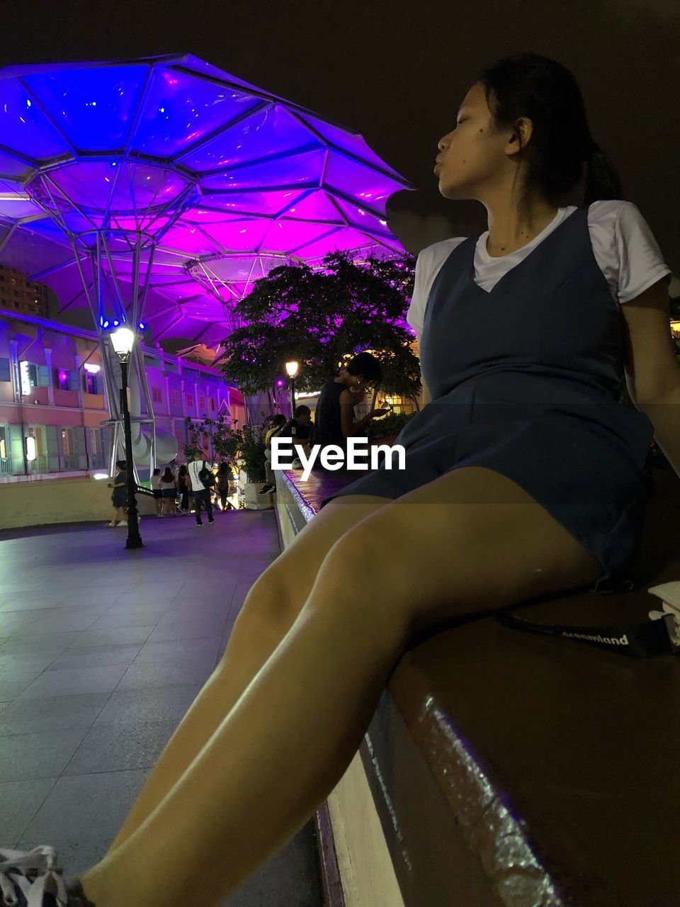 SIDE VIEW OF WOMAN SITTING IN ILLUMINATED PARK