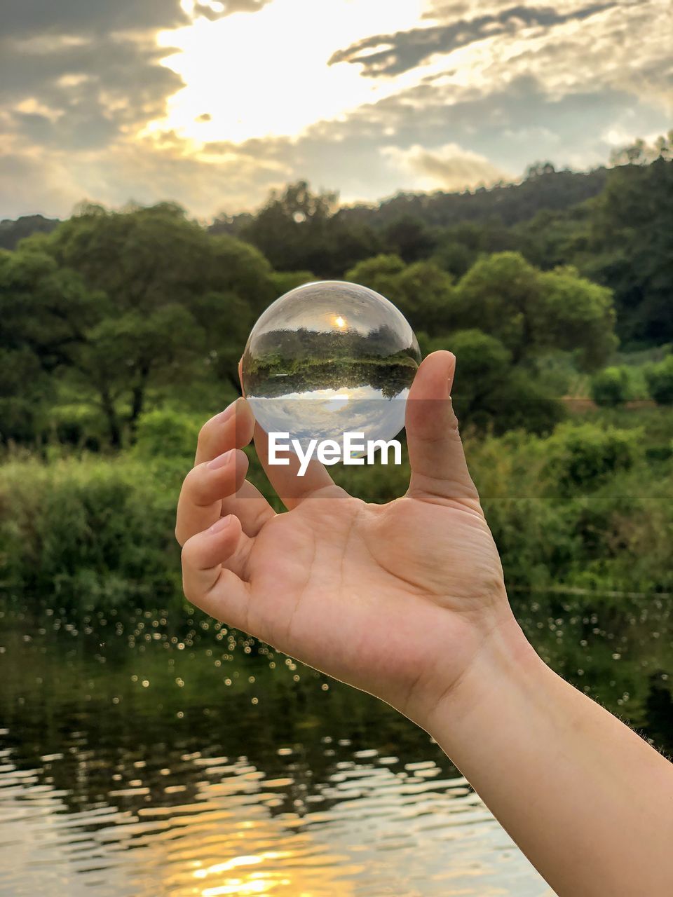 Cropped image of person holding crystal ball over lake
