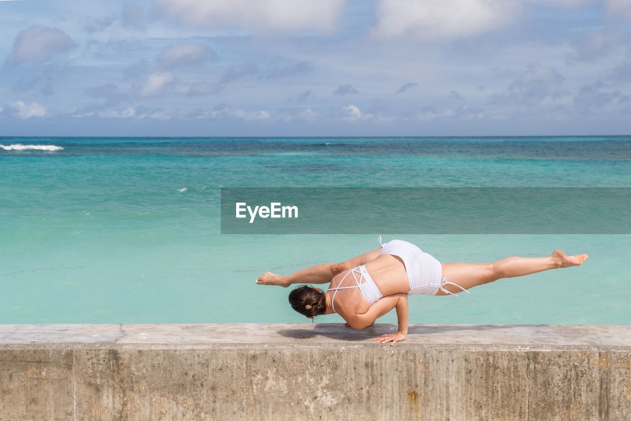 Woman exercising on retaining wall against sea