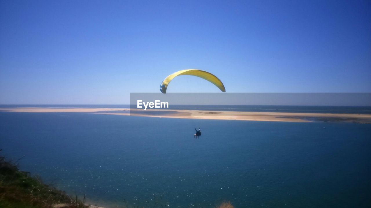 PERSON PARAGLIDING OVER SEA AGAINST BLUE SKY