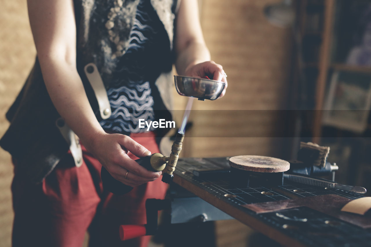 The master woman near the bench works with tools, on the torch boils water with a metal plate.