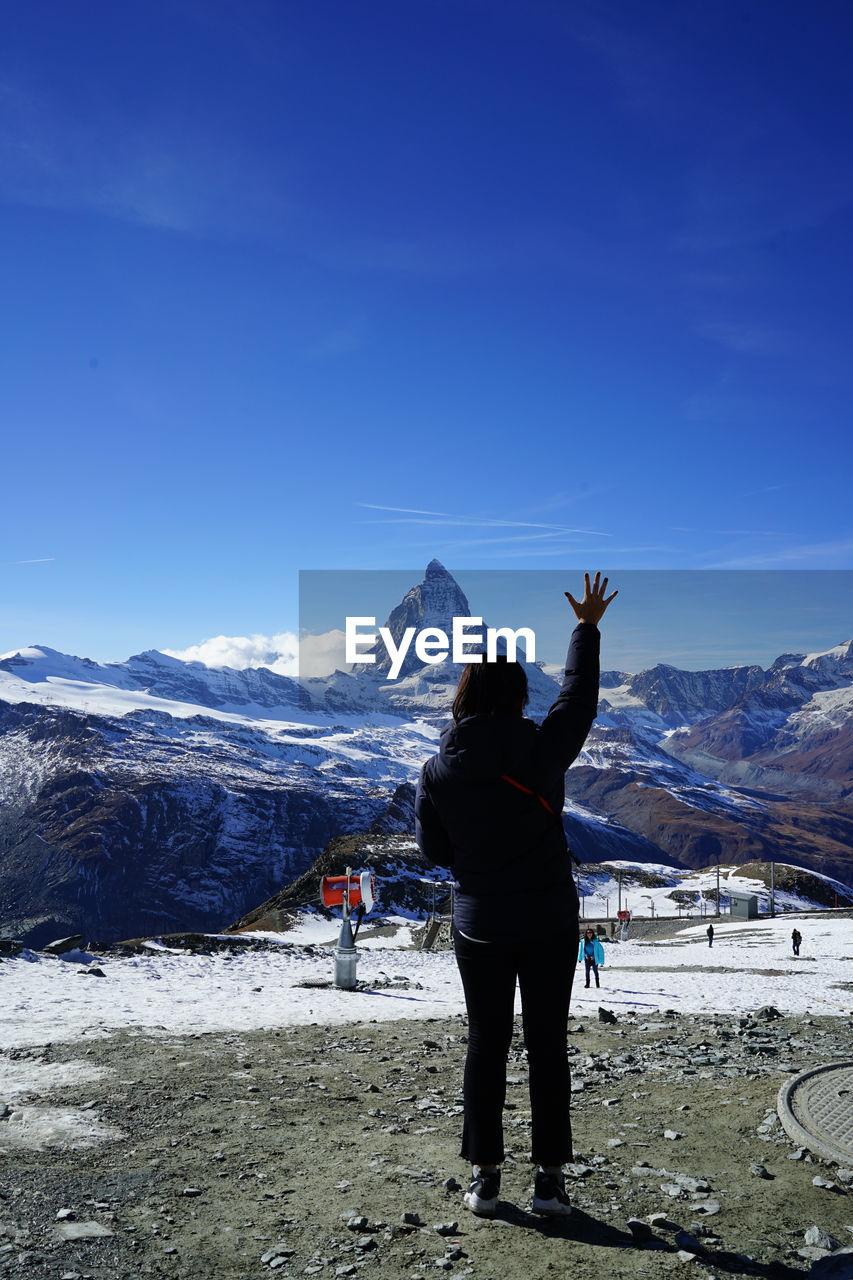 Rear view of woman with arm raised standing by snowcapped mountains