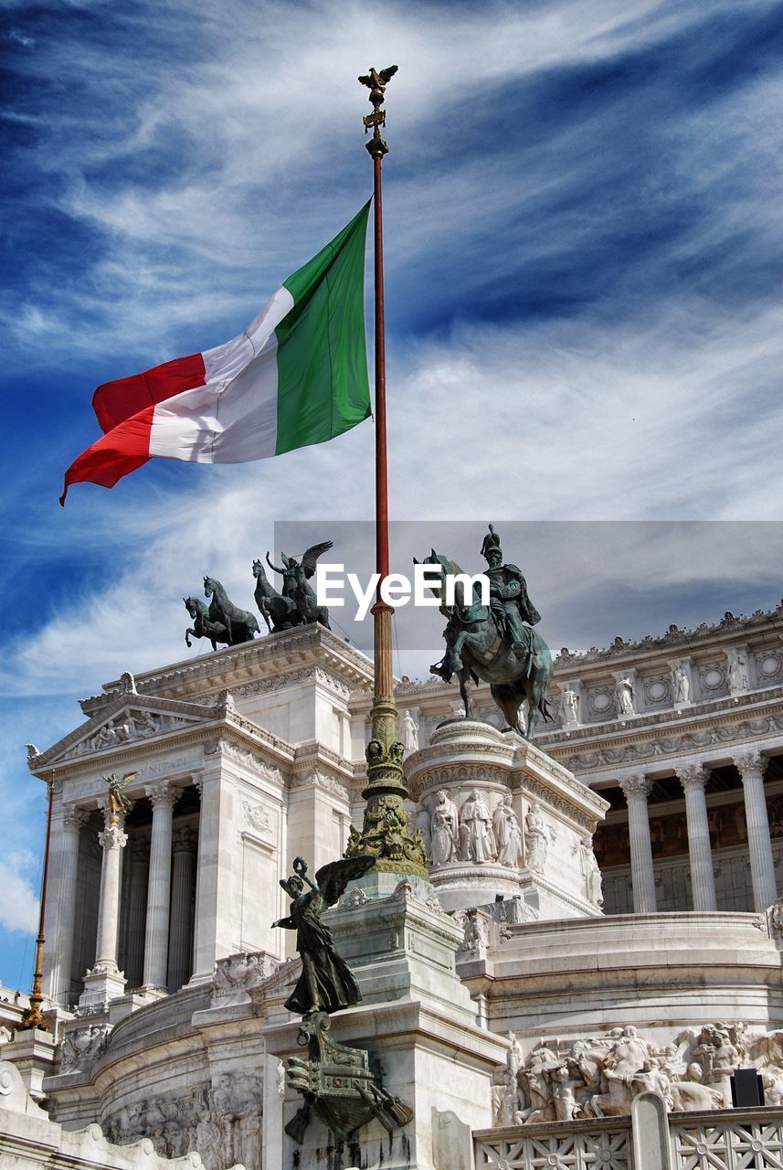 Low angle view of flag and statue at altare della patria against cloudy blue sky