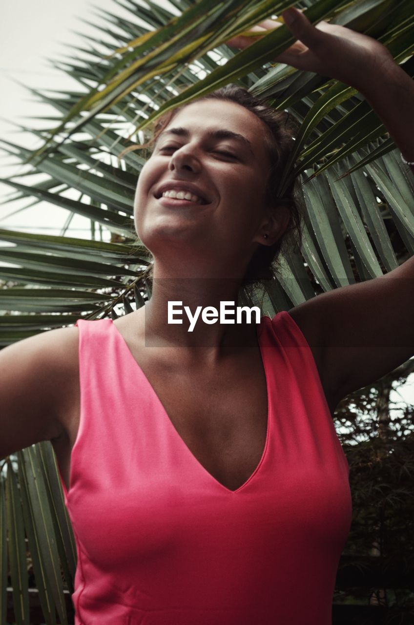 Close-up of smiling young woman standing by tree outdoors