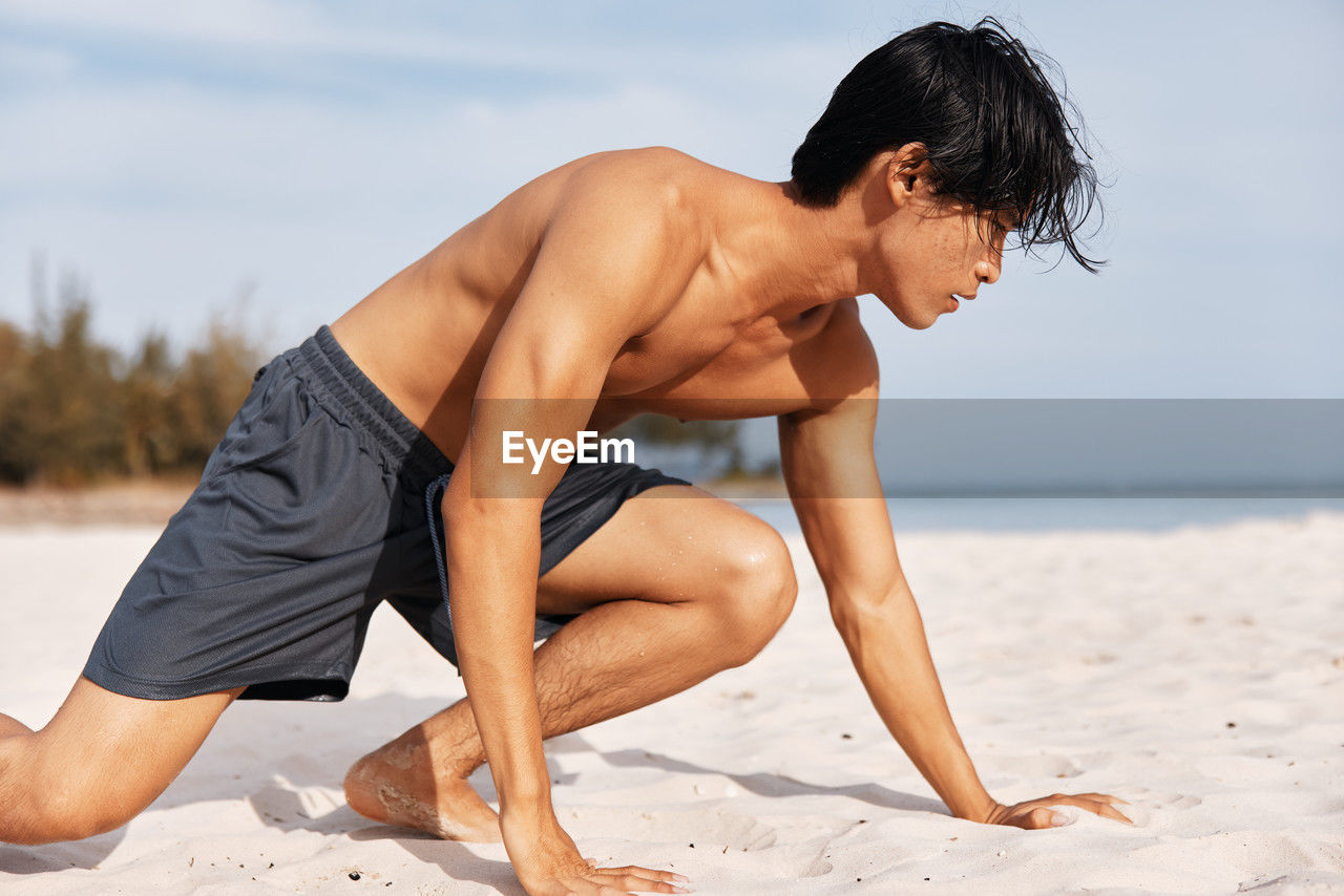 low section of shirtless man exercising on beach
