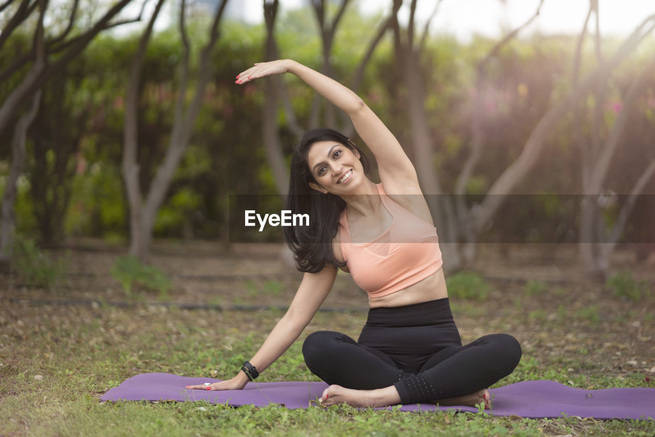 Full length portrait of woman with arms raised on mat in park