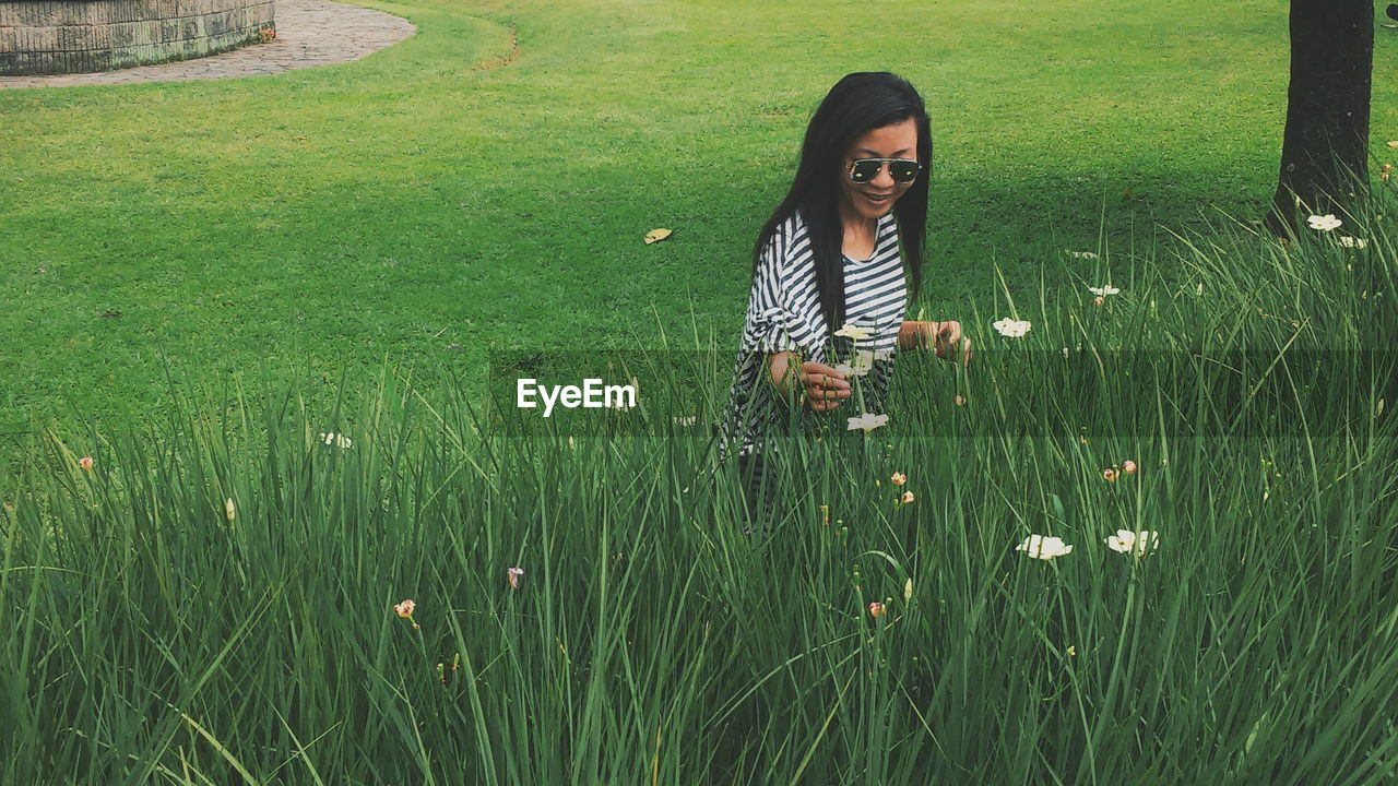 Mid adult woman picking flowers on grassy field