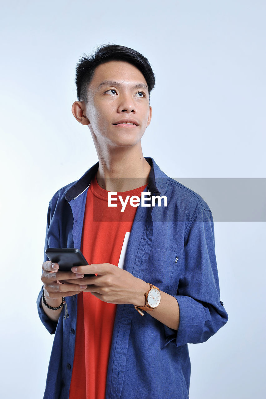 Potrait of handsome young asian man holding a smart phone and wear wristwatch with pretty smiling look at the copy space