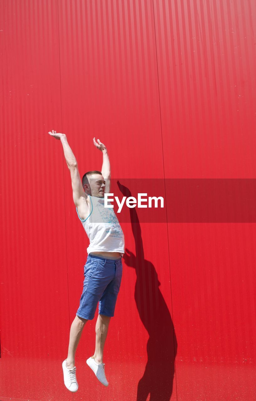 Full length of man jumping against red wall