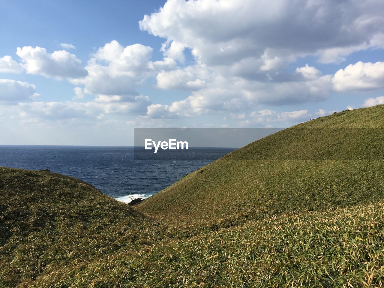 SCENIC VIEW OF SEA BY AGRICULTURAL LANDSCAPE AGAINST SKY