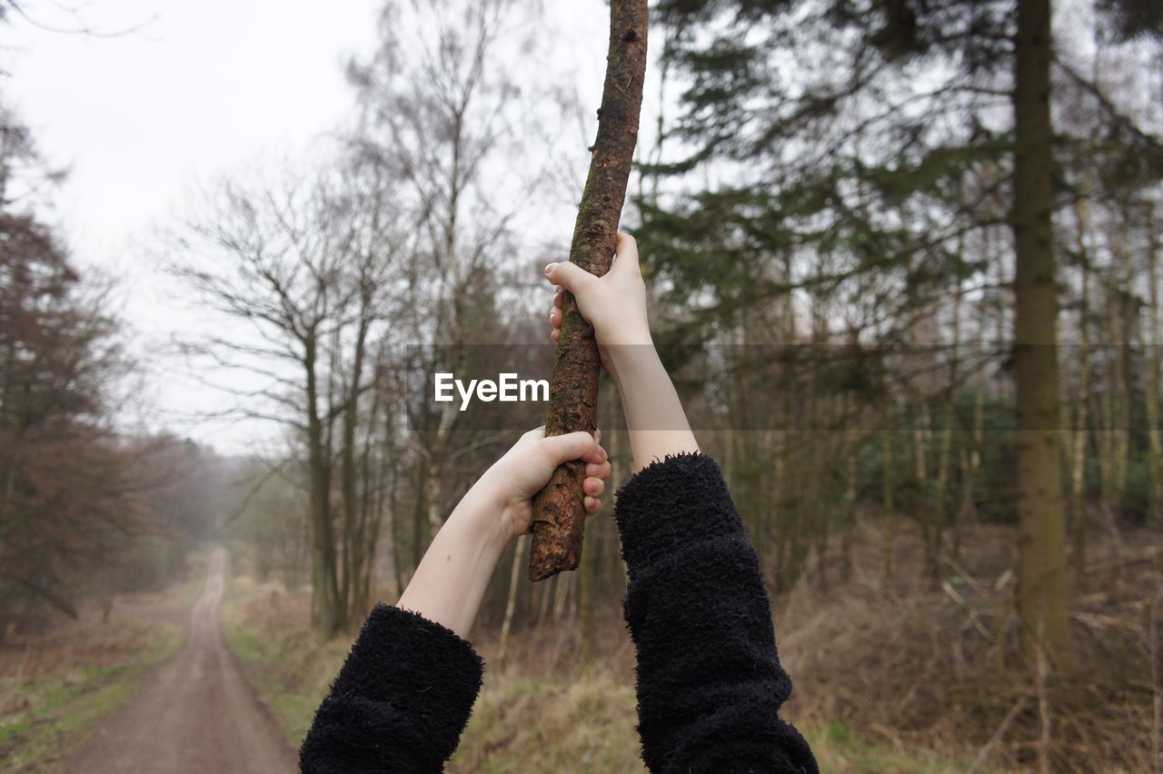 Cropped image of woman holding branch while standing on footpath